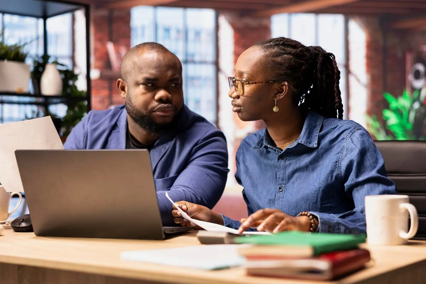 A Black man and a Black woman at a desk reviewing financial documents and keeping track of expenses.