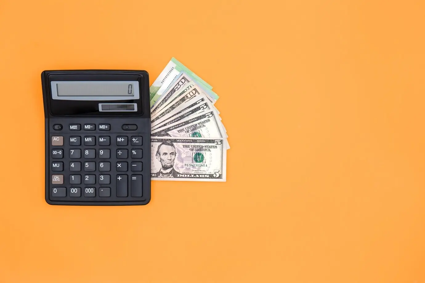 A calculator and dollar bills against an orange background with copy space.