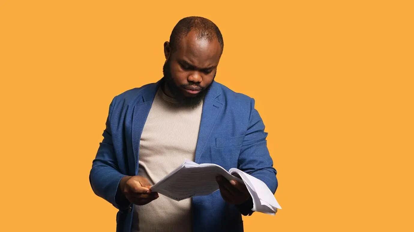 A man flips through report files and throws them in anger, feeling overworked.